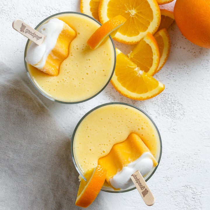 two completed Orange Creamsicle Smoothies in glass jars with oranges in the background