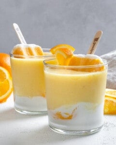two completed Orange Creamsicle Smoothies in glass jars with oranges in the background