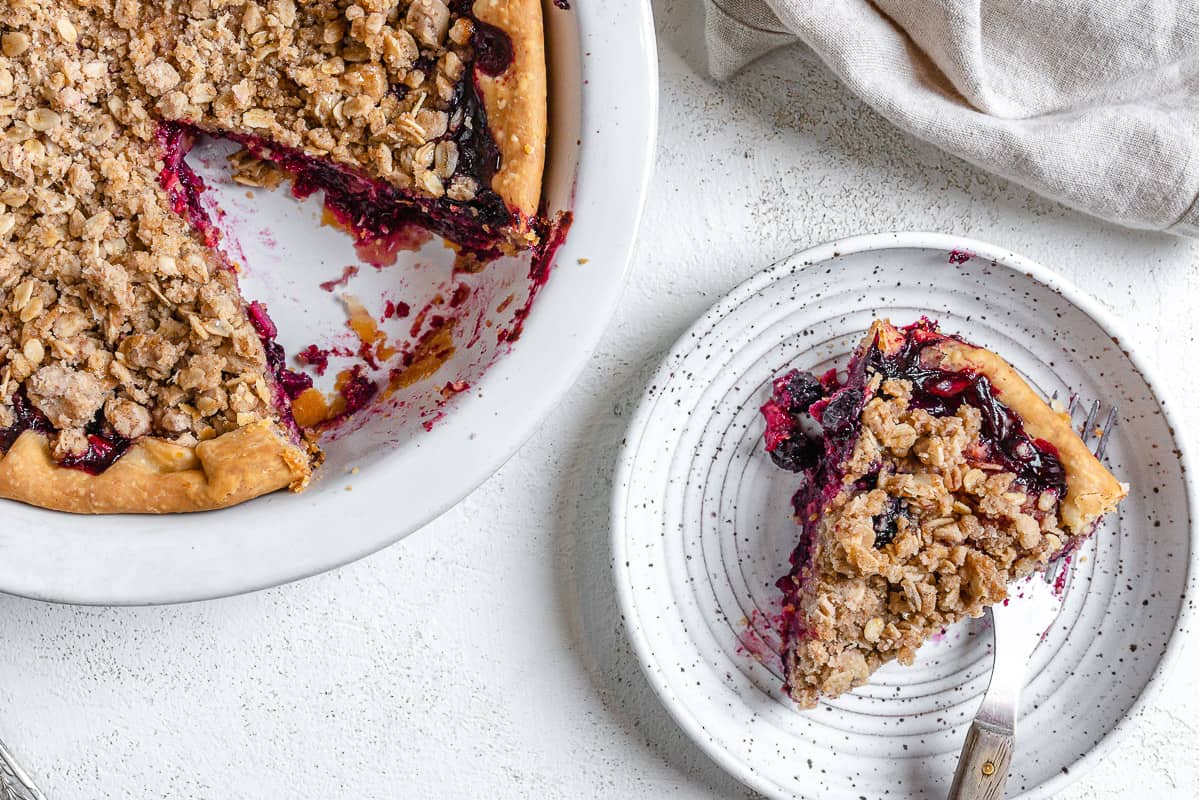 completed Mixed Berry Crumb Pie with a piece plated on a small white plate