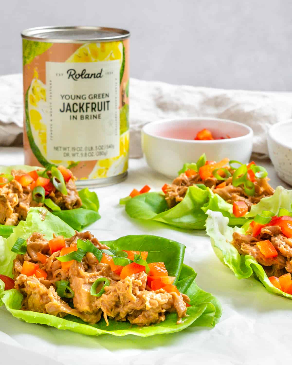 several completed Jackfruit Lettuce Cups spread out on a white surface with a jan of jackfruit in the background