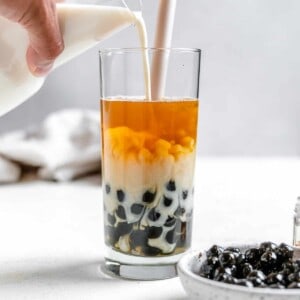 process shot of pouring boba tea into a glass with ingredients in the background