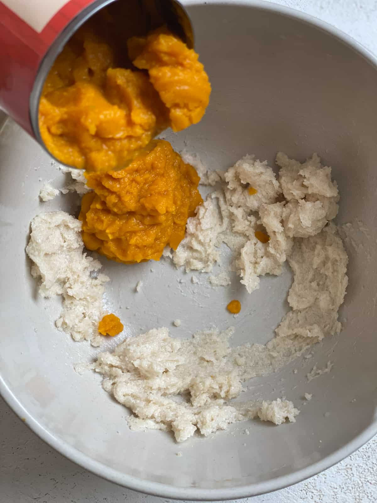 process of adding pumpkin to bowl of ingredients in a white bowl