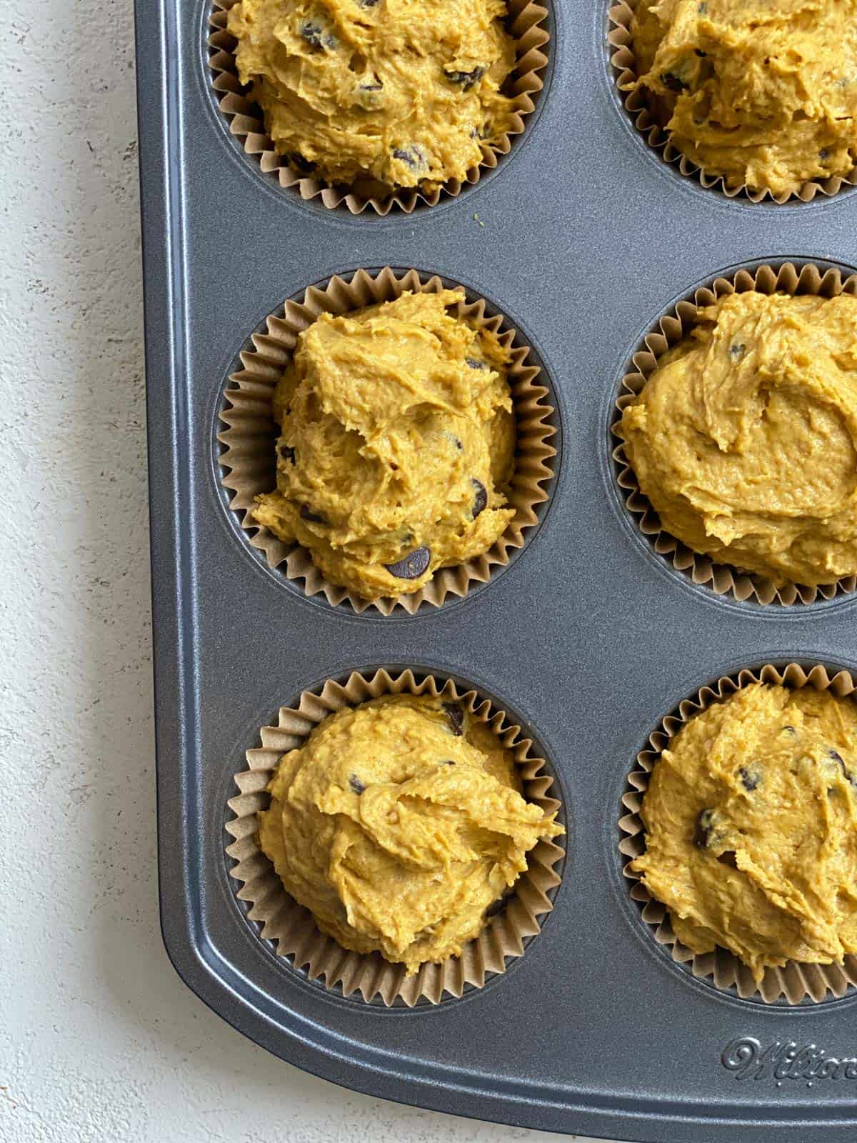 process of adding unbaked muffin batter to muffin tin