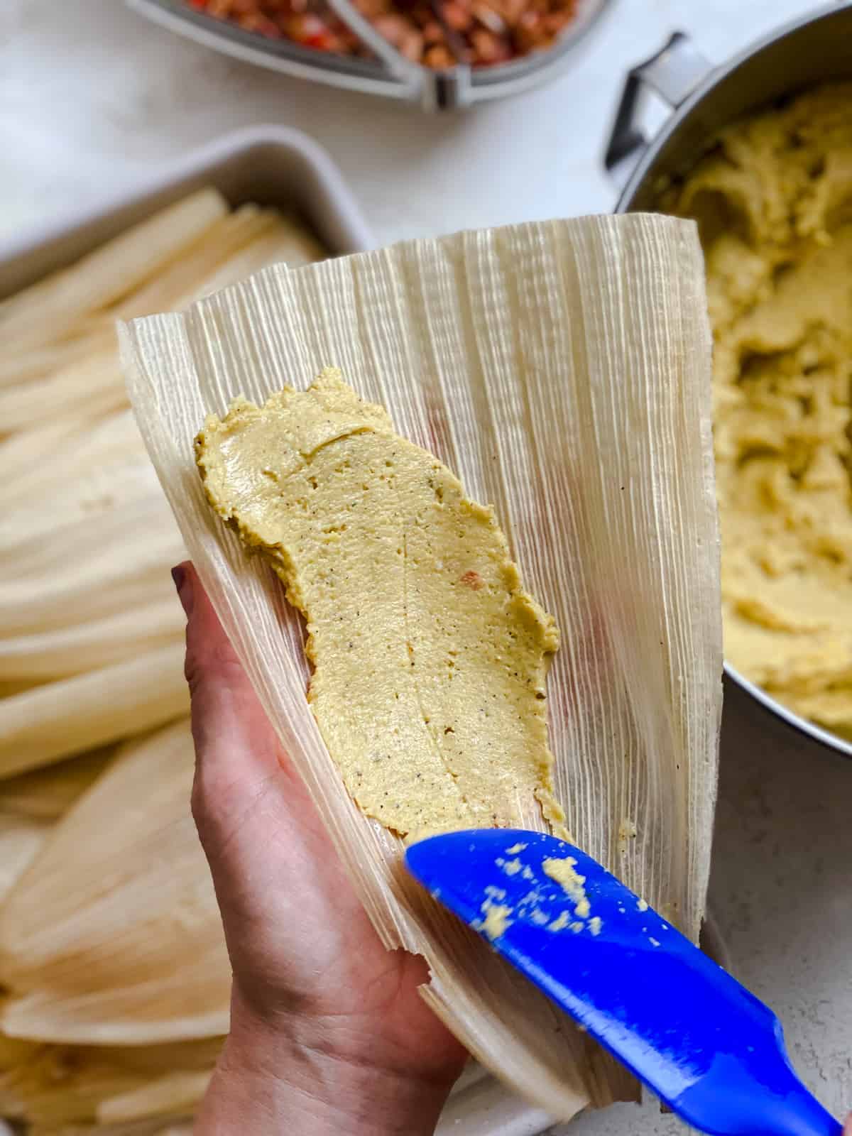 process shot of spreading tamales filling mixture into corn husk