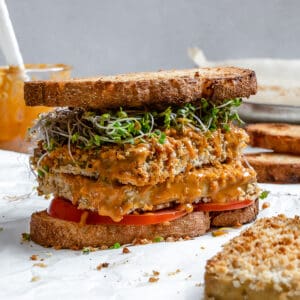 completed Easy Crispy Buffalo Tofu Sandwich against a white background with ingredients in the back