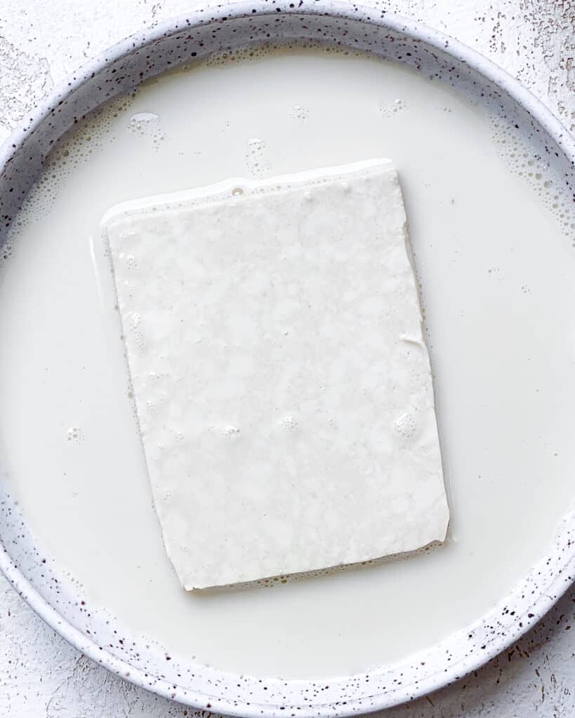 process shot of dipping tofu into plant-based milk