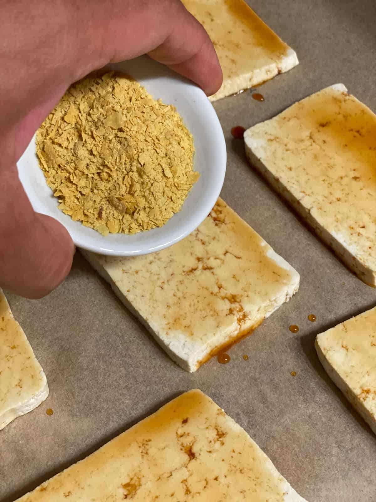 process shot of adding nutritional yeast to tofu slices