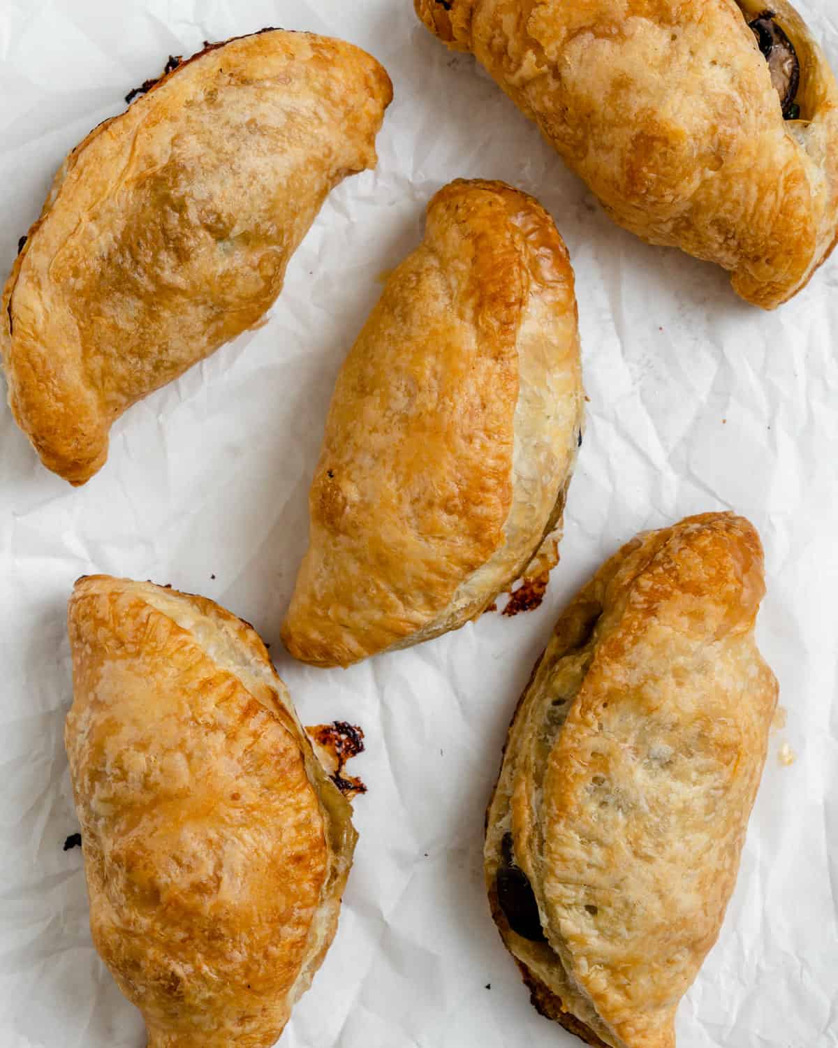 several completed Spinach and Mushroom Puffs [Vegan Hand Pies] scattered on a white surface