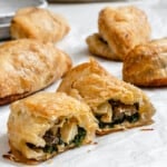 several completed Spinach and Mushroom Puffs [Vegan Hand Pies] scattered on a white surface