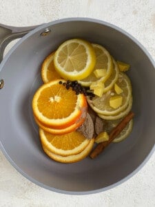 sliced orange, lemon, ginger, cinnamon stick, cardamom pods, and peppercorns in a saucepan for lemon cinnamon ginger tea