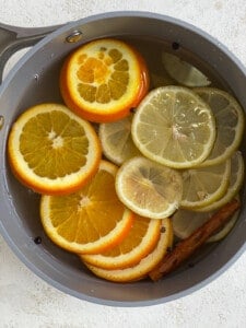water poured over citrus slices and spices in a saucepan for lemon cinnamon ginger tea