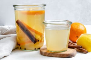 two jars of lemon cinnamon ginger tea with an orange, lemon, and cinnamon sticks