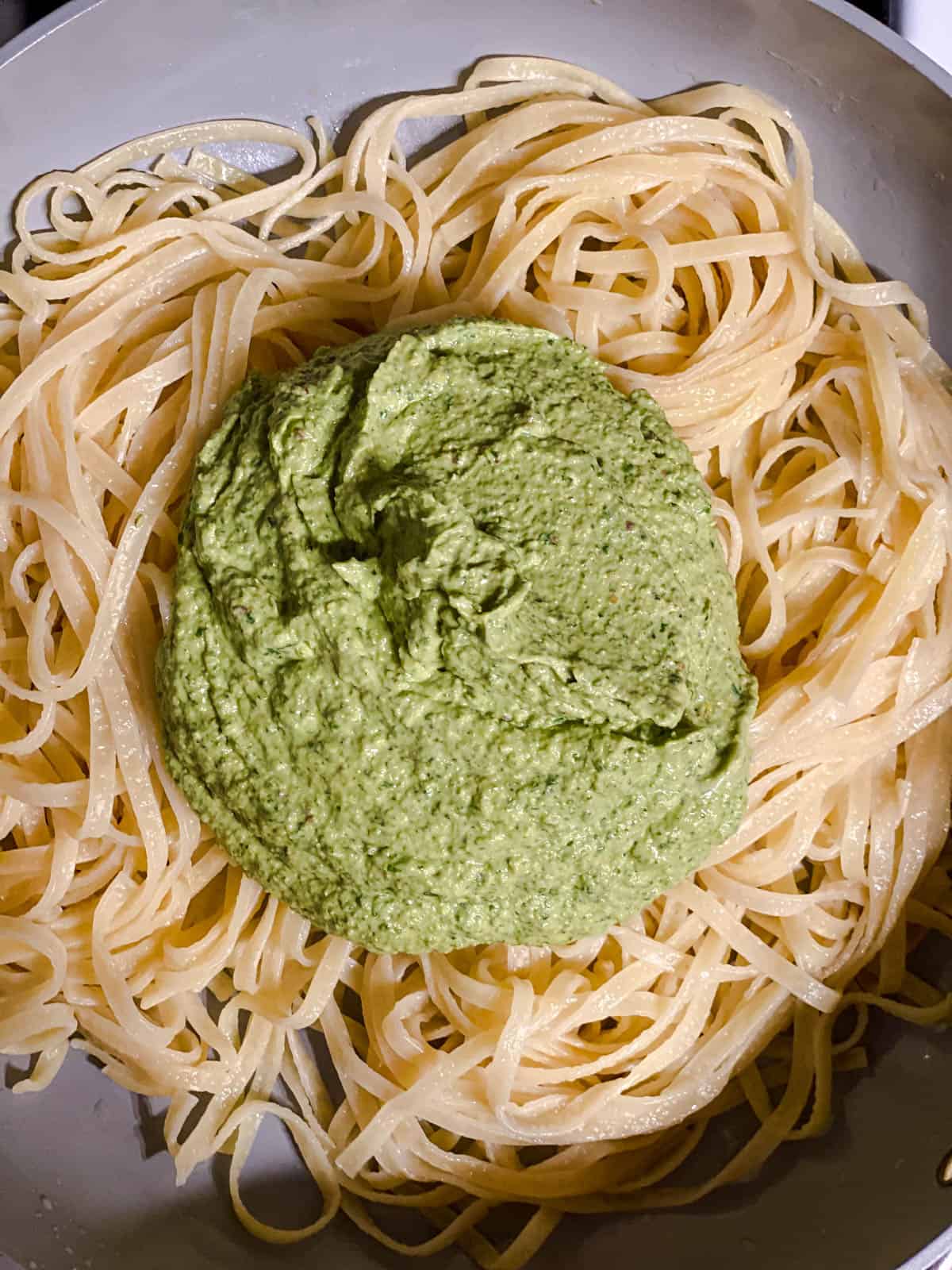 process shot of avocado pesto being added to noodles