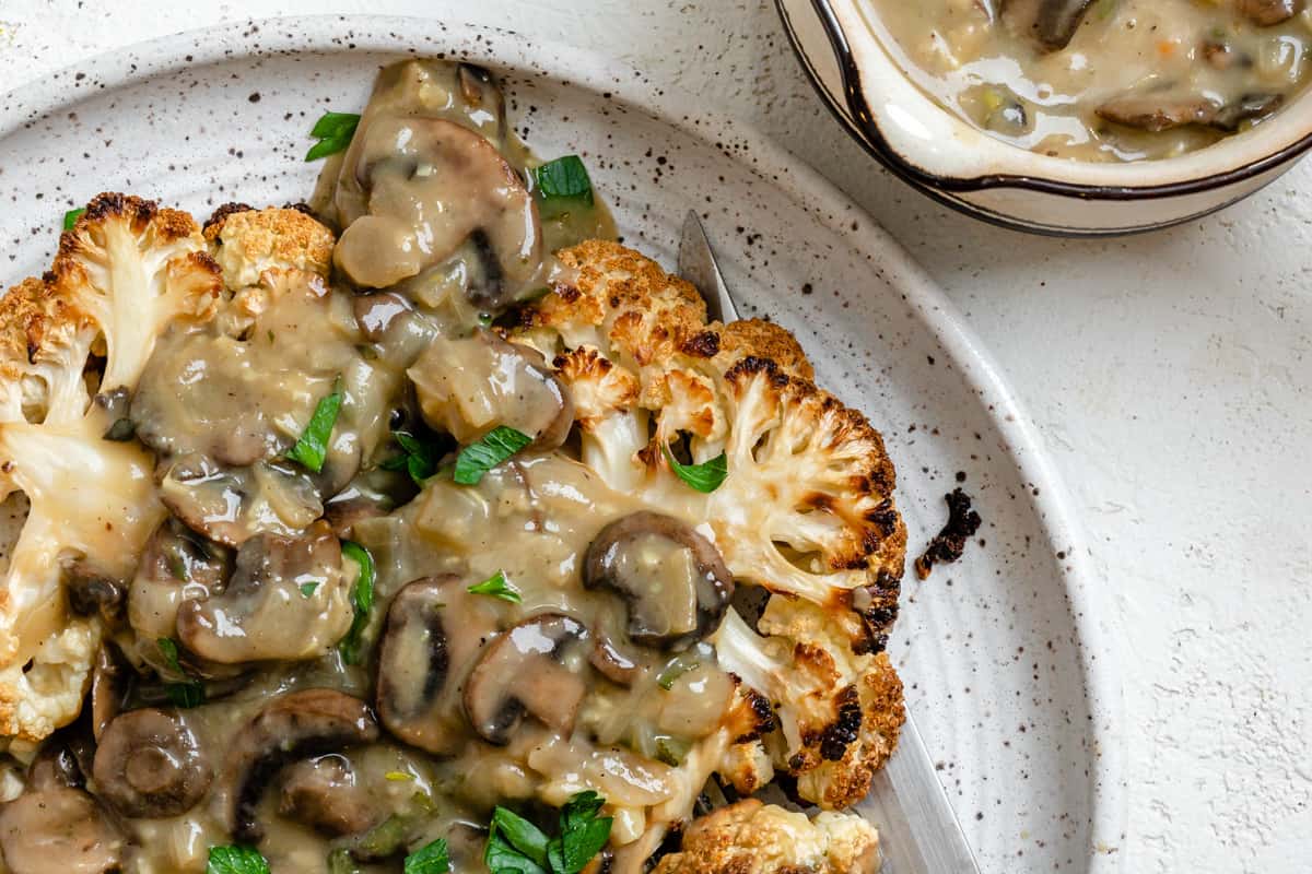 Close-up of crispy roasted cauliflower steaks topped with mushroom gravy and parsley.