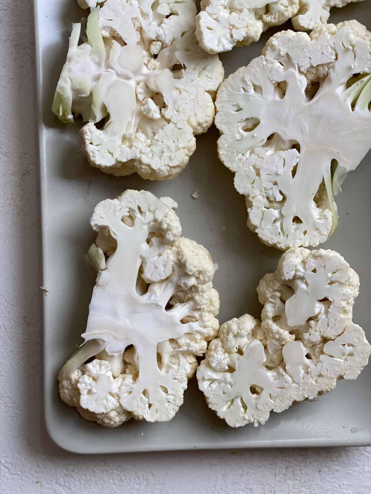 Raw cauliflower cut into thick steaks on a white tray.