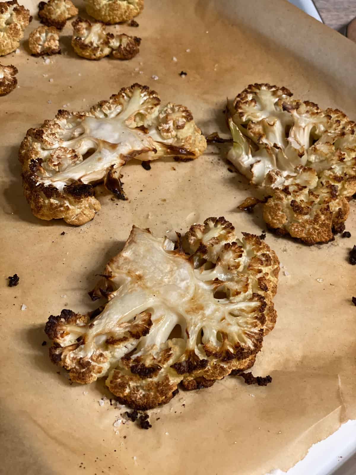 Golden roasted cauliflower steaks with crispy edges on a parchment-lined baking sheet.