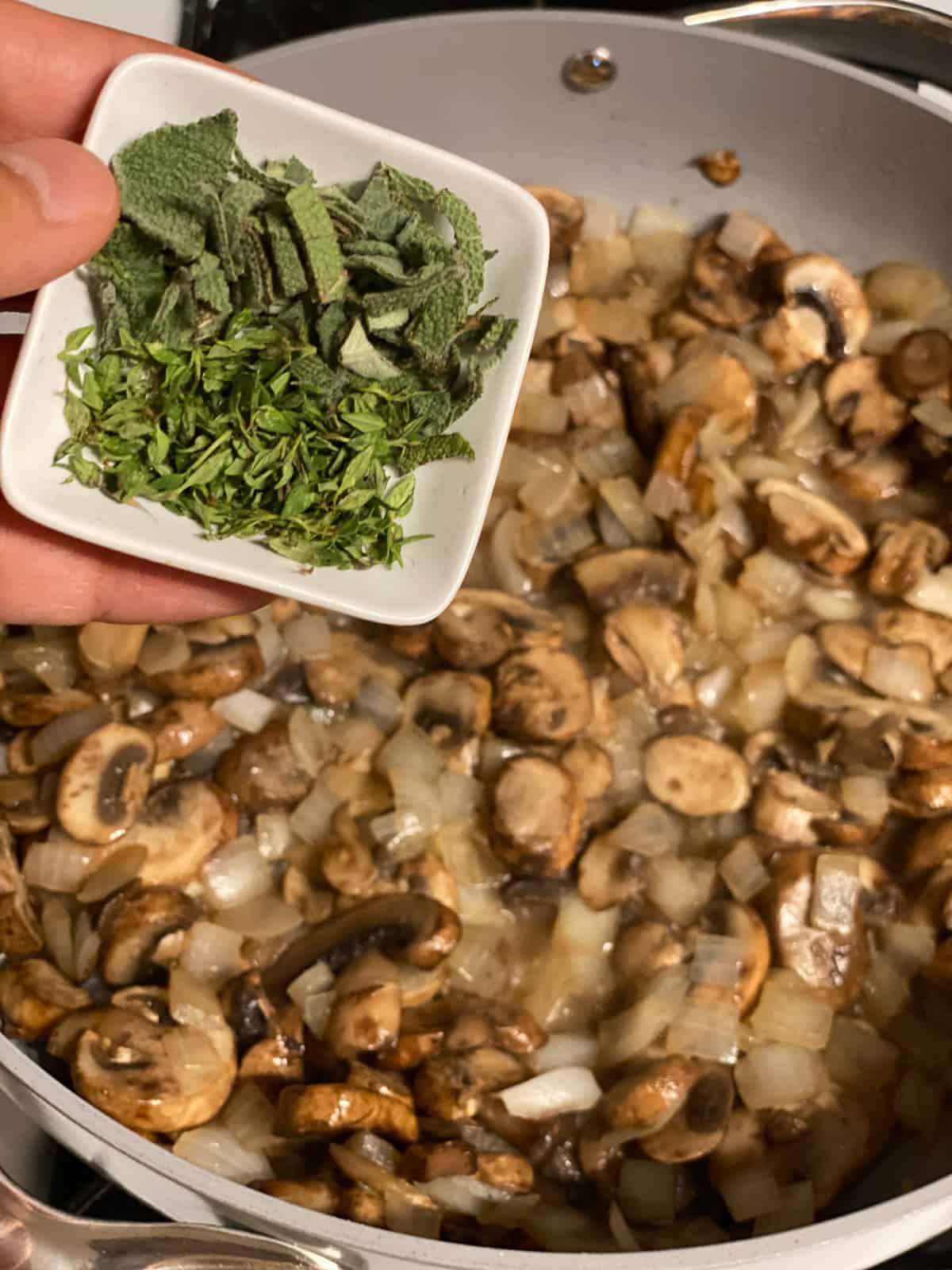 Fresh chopped sage being added to mushrooms and onion in a skillet.