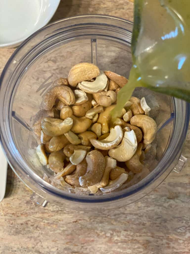 process shot of adding veggie broth to blender of cashews