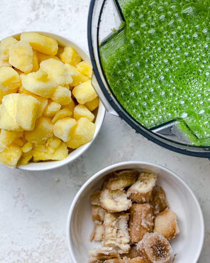 blended kale alongside bowl of pineapple and banana