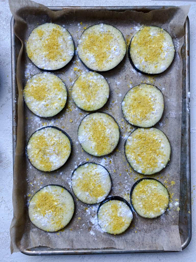 process shot post adding seasoning to eggplant slices on baking tray