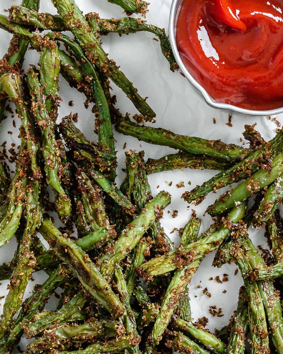 completed Crispy Green Bean Fries scattered on a white surface alongside ketchup