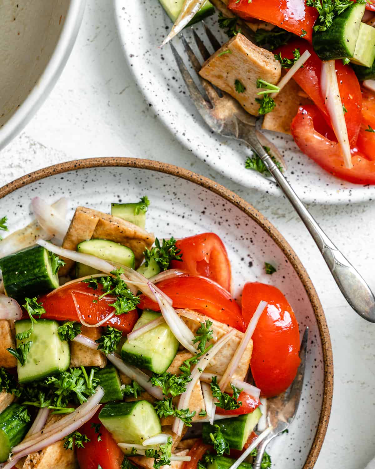 Ready panzanella salad on two plates in front of a white surface