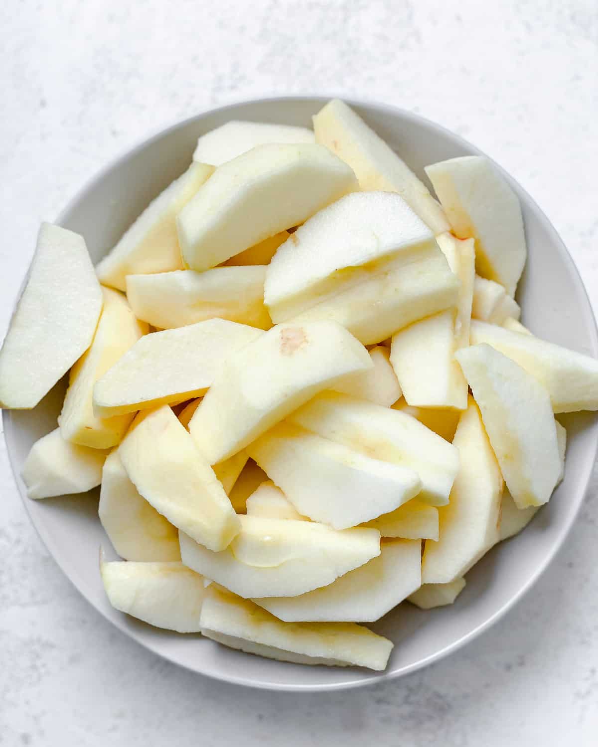 sliced apples in a white bowl against a white background