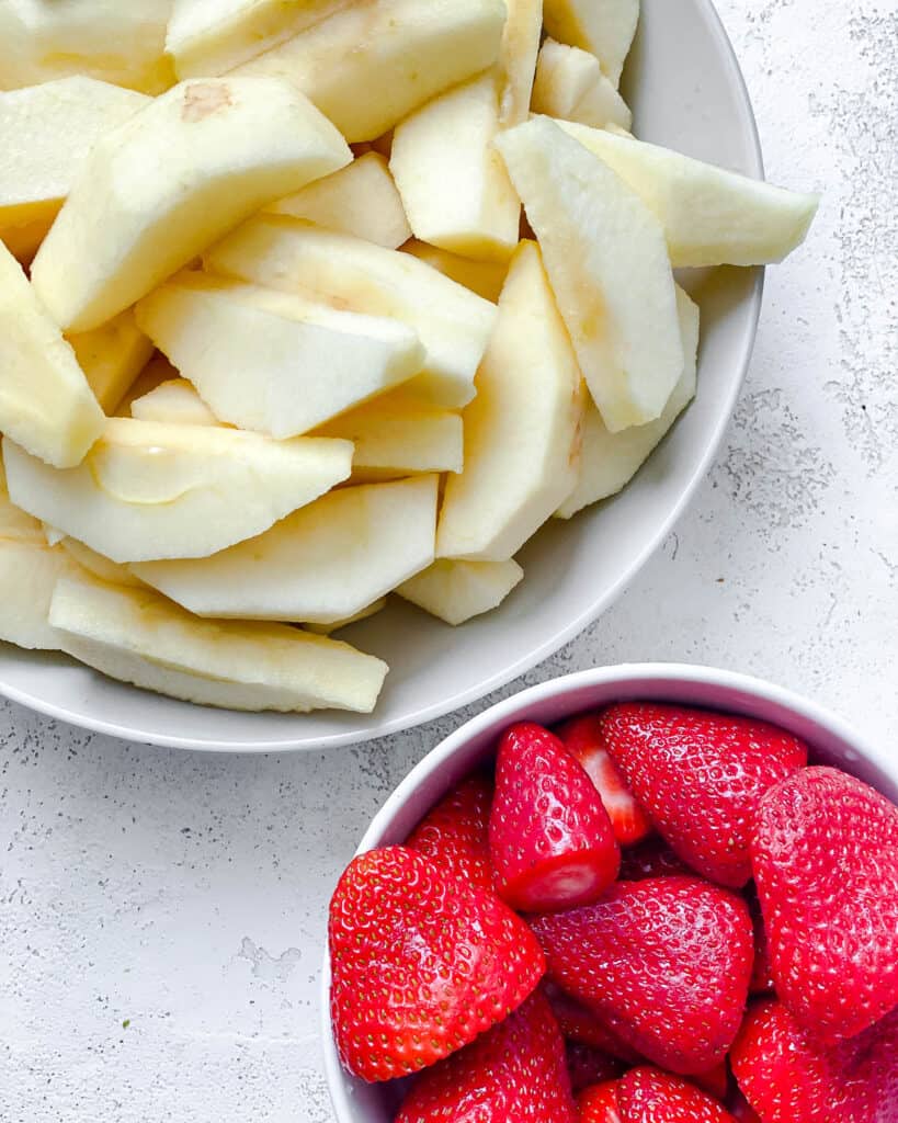 sliced apples and strawberries in a white bowl against a white background
