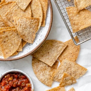completed Air Fryer Tortilla Chips plated alongside chips against a white surface with salsa on the side
