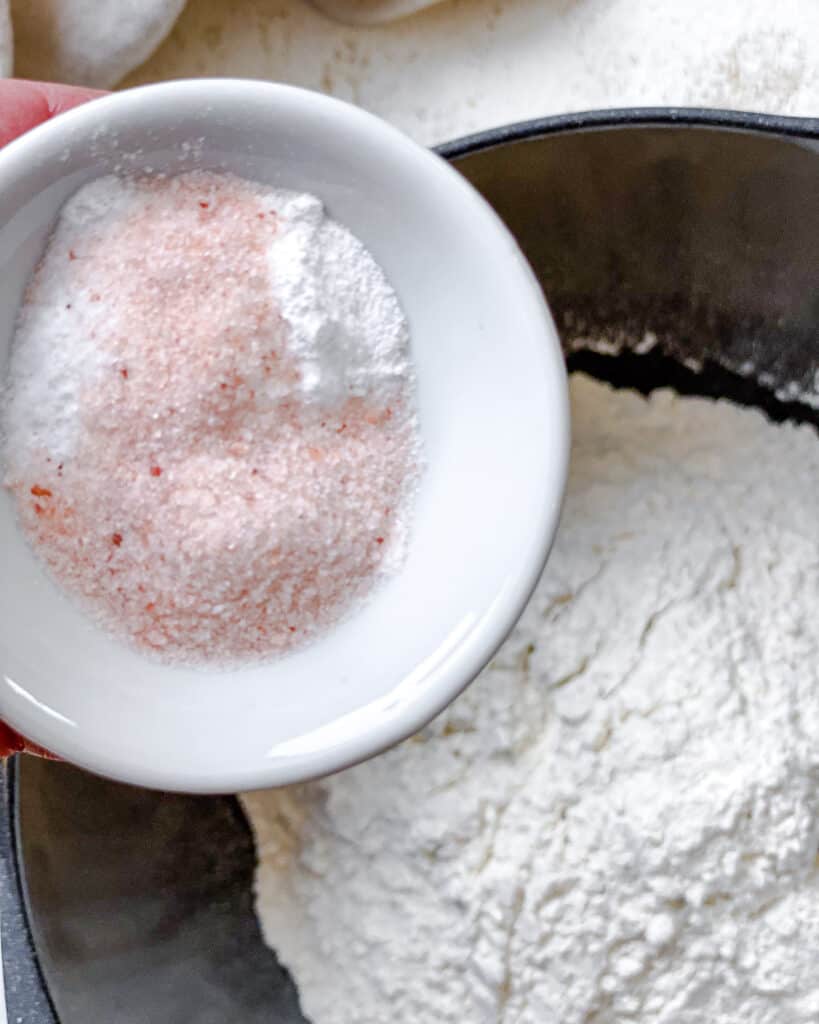 process shot of adding salt and baking soda and powder to bowl of flour