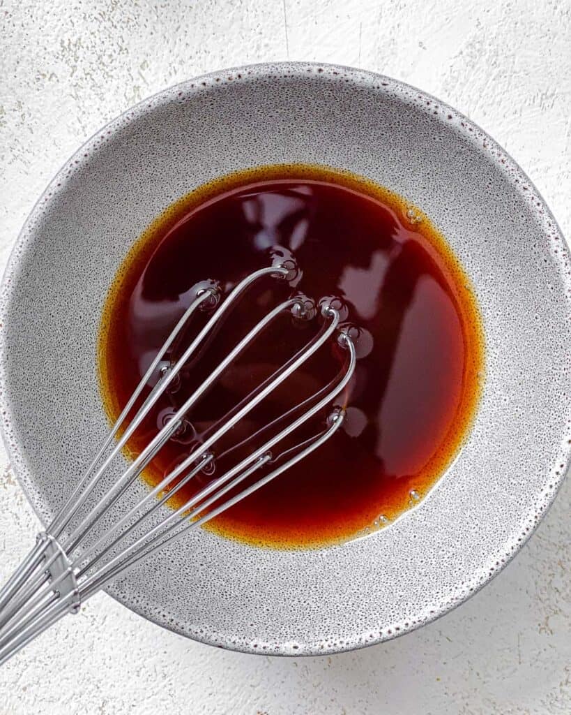process shot of mixing sauce in a white bowl with whisk