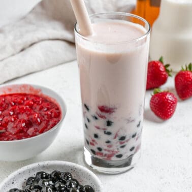 completed Strawberry Boba Tea in a glass cup with ingredients in the background