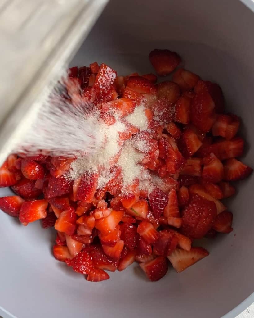 process of adding sugar to strawberries in bowl