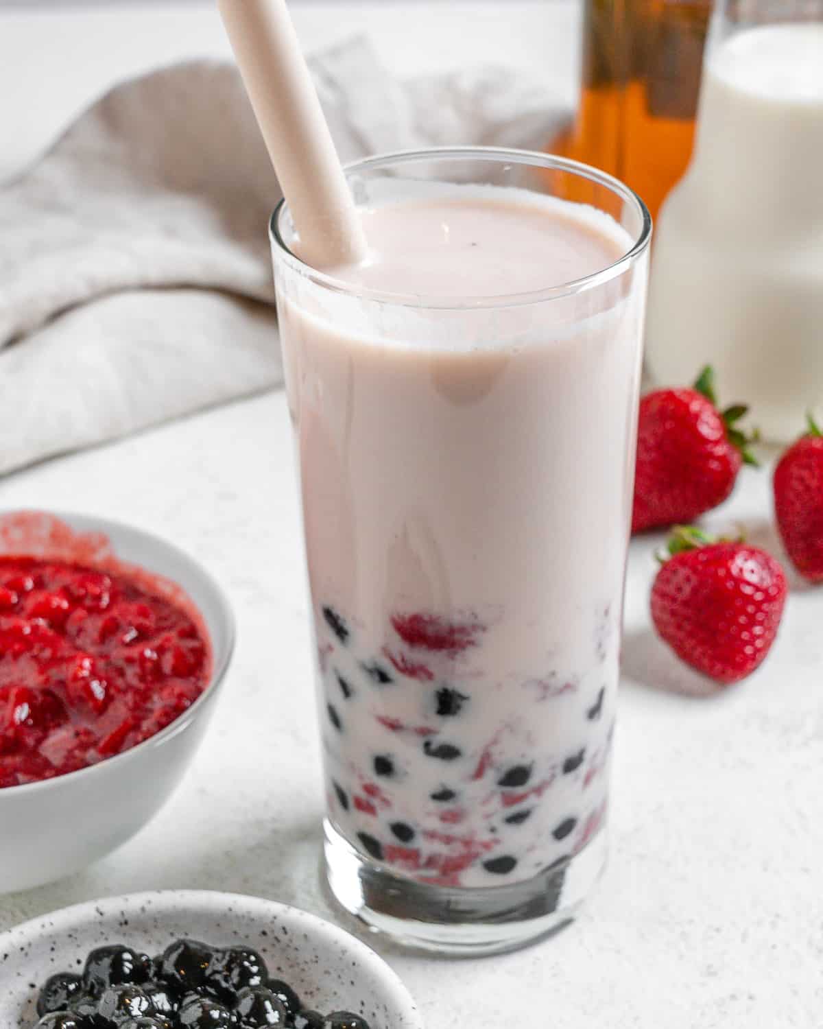 completed Strawberry Boba Tea in a glass cup with ingredients in the background