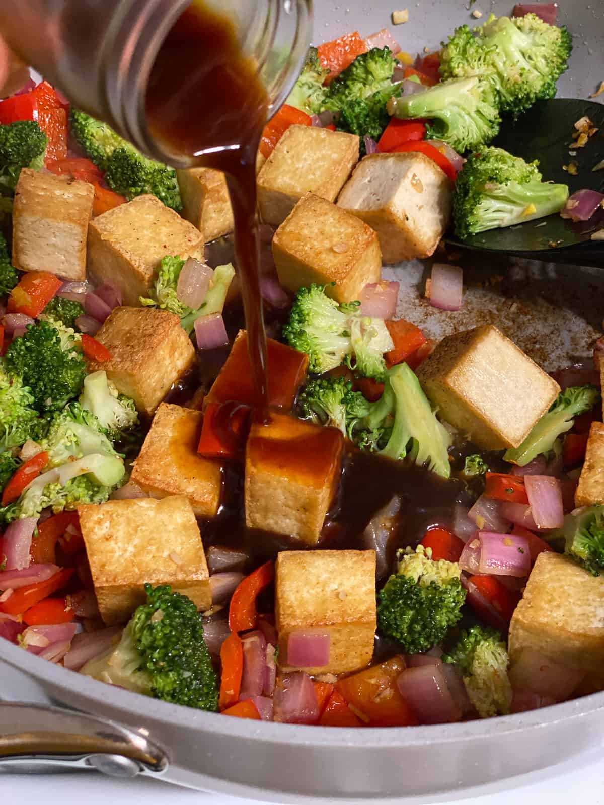 process shot of adding sauce to pan of tofu and veggies
