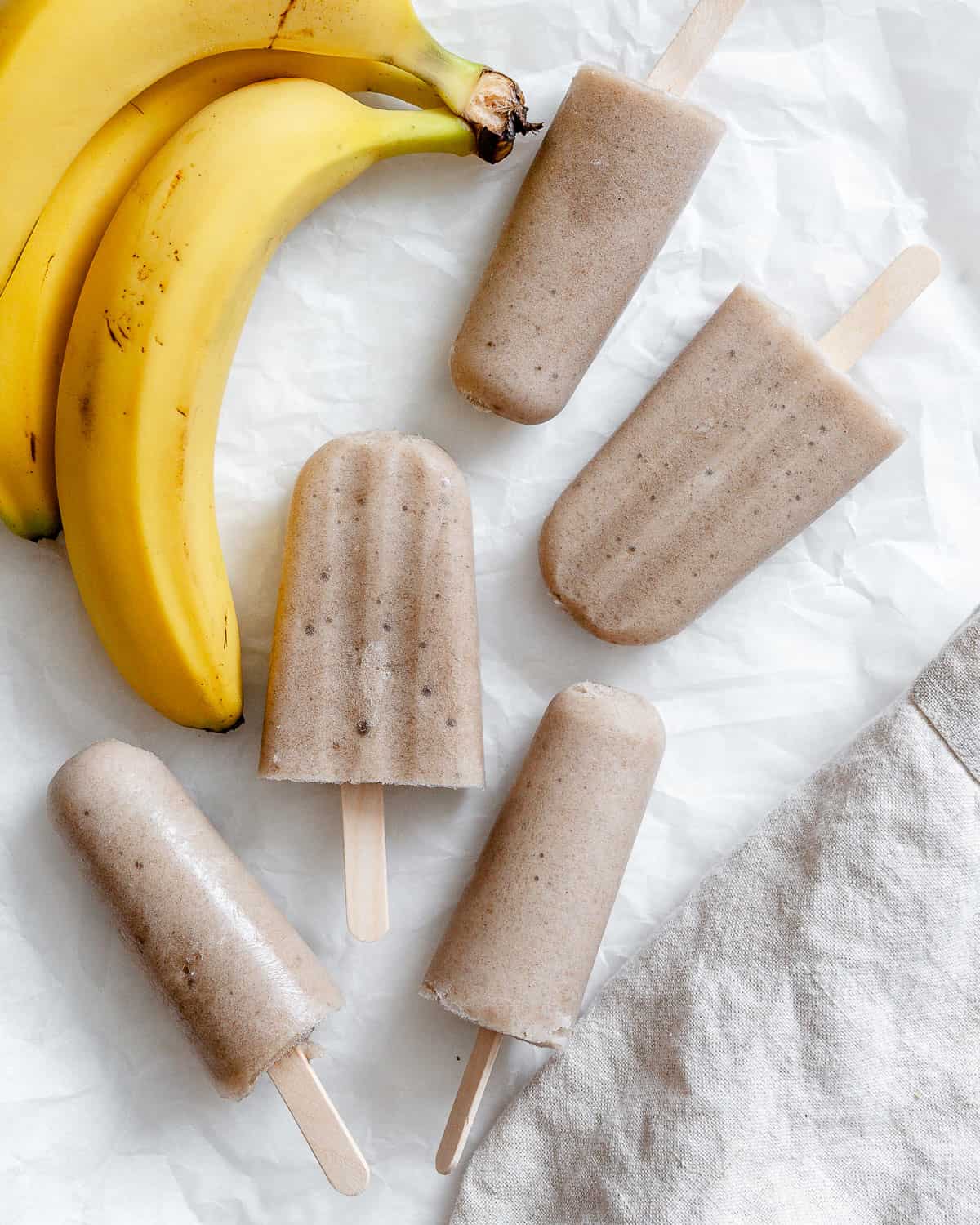 completed Healthy Banana Popsicles a،nst a white surface alongside bananas