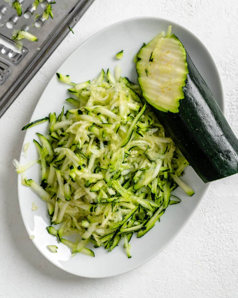process of grating zucchini in a white tray against a white background