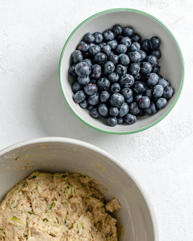 bowl of blueberries alongside white mixing bowl against white background