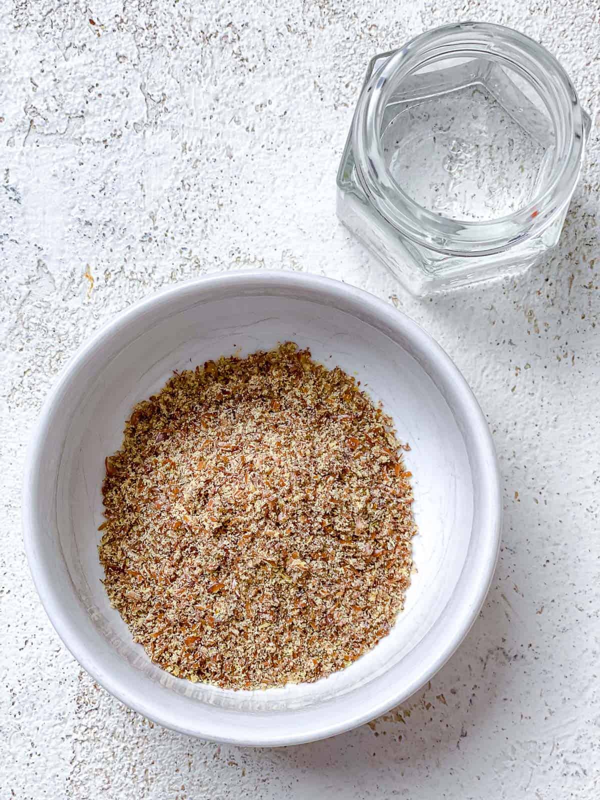 bowl of flaxseed and water measured out on a white surface