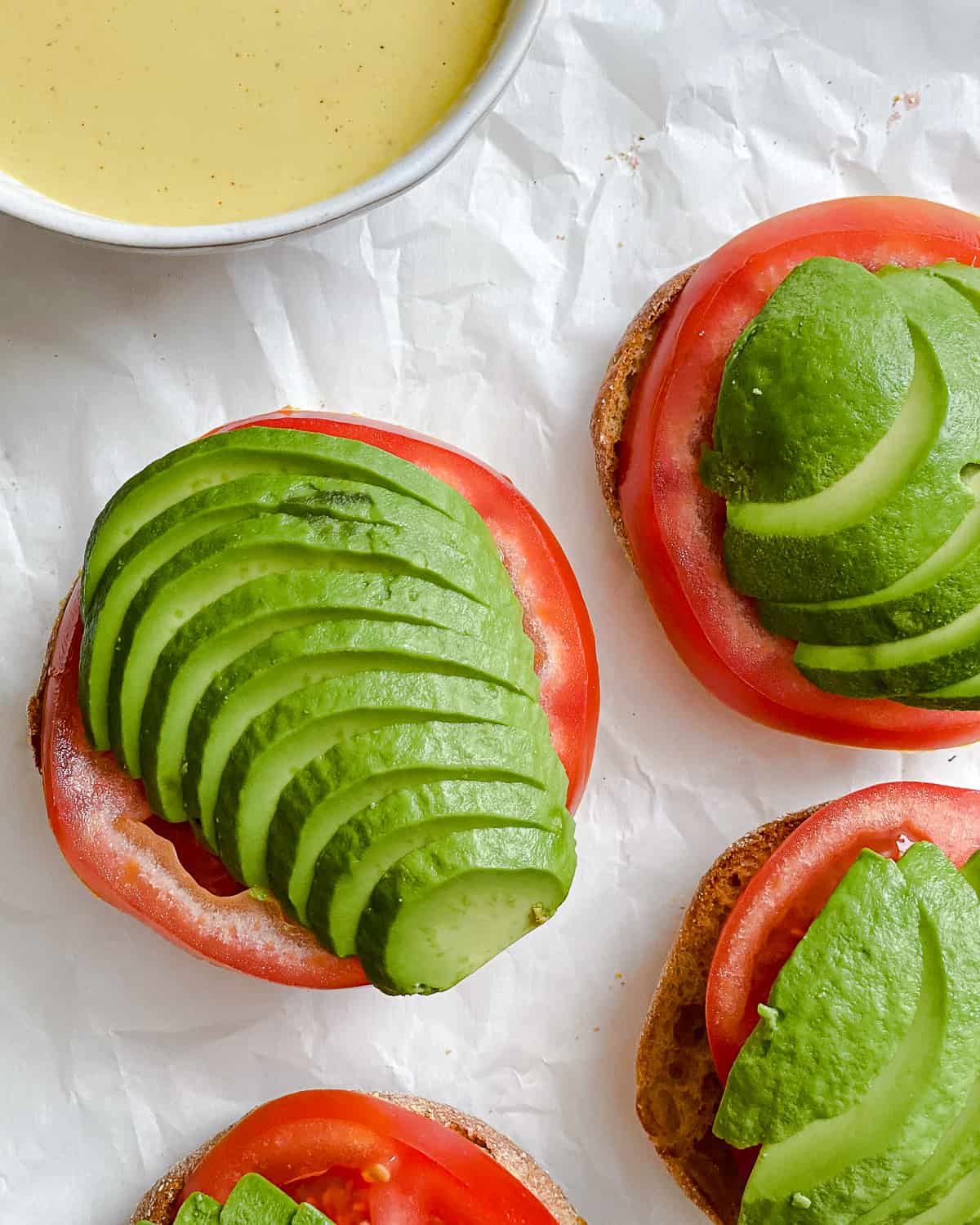 Process shot of adding tomato and avocado slices to the sandwich