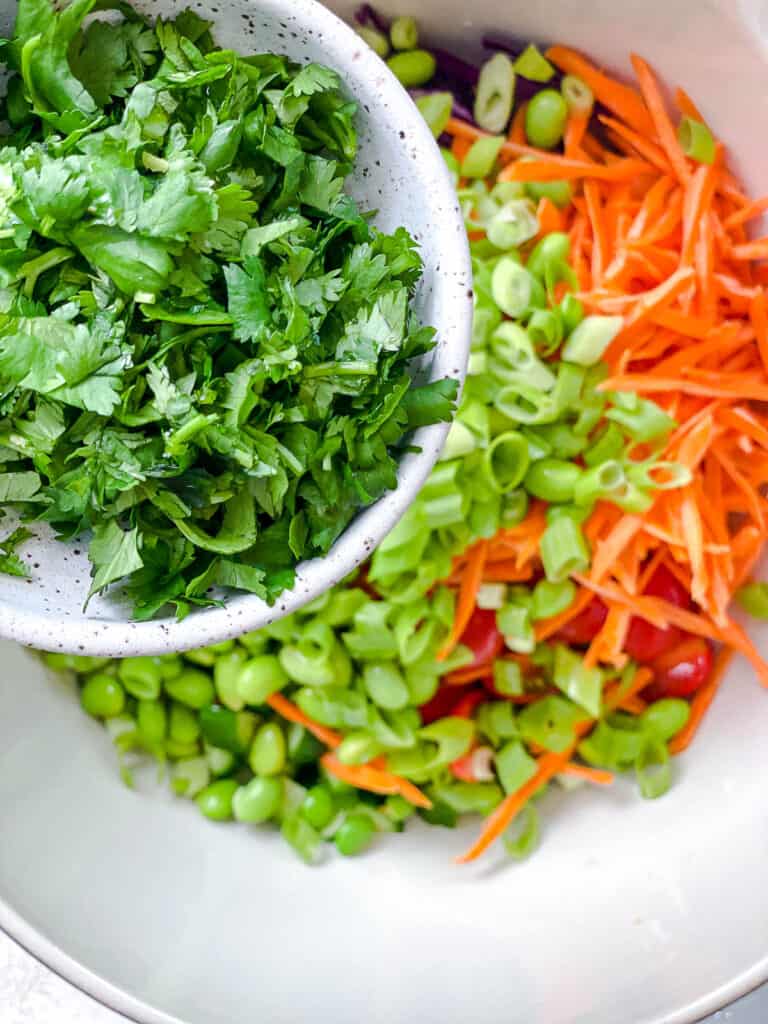 process shot of adding cilantro to bowl of veggies