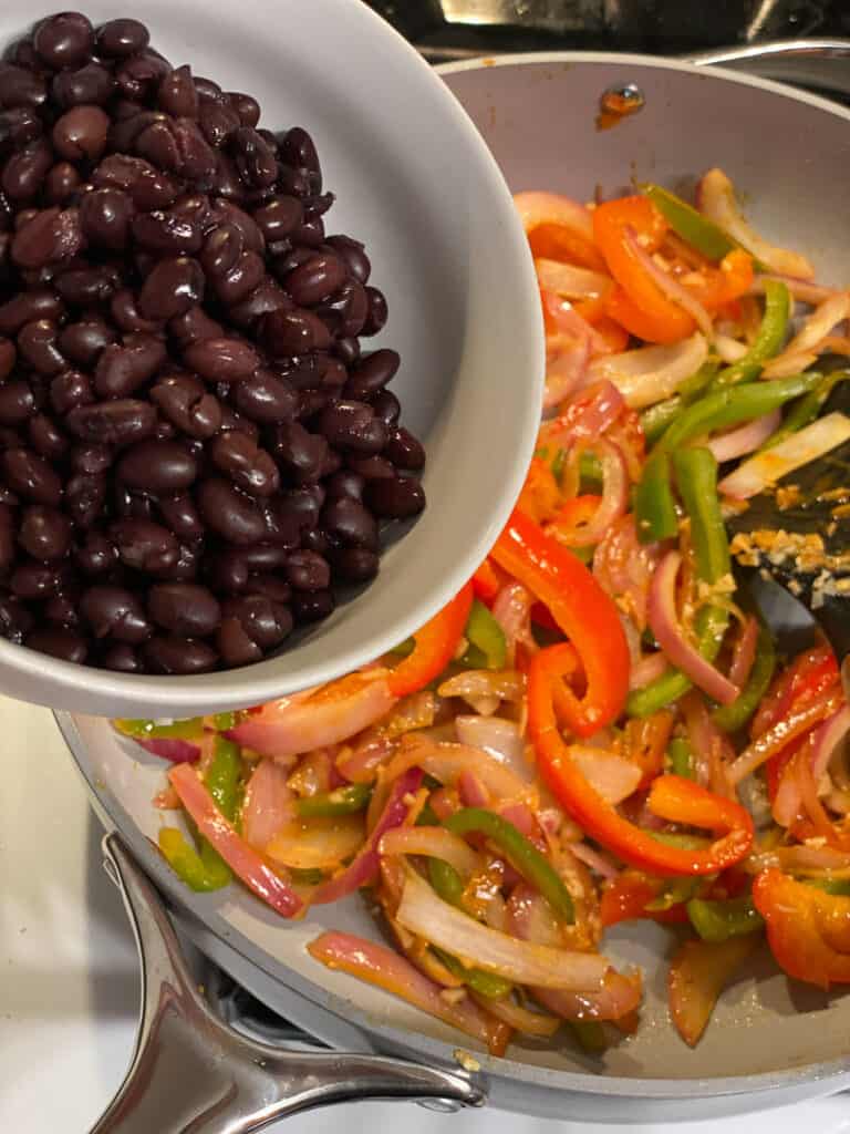 process of beans being poured into pan of veggies