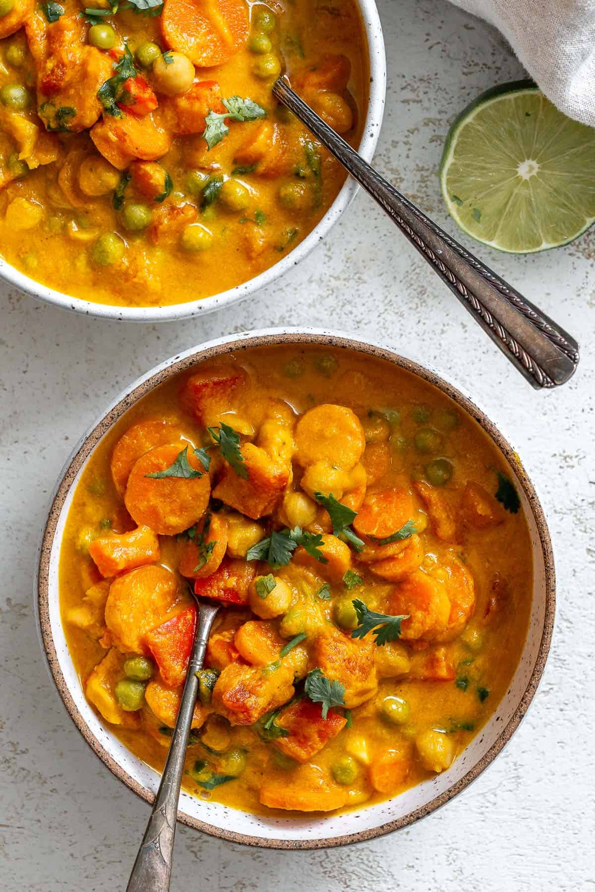 two bowls of completed Creamy Chickpea and Carrot Curry in a bowl a،nst a white surface