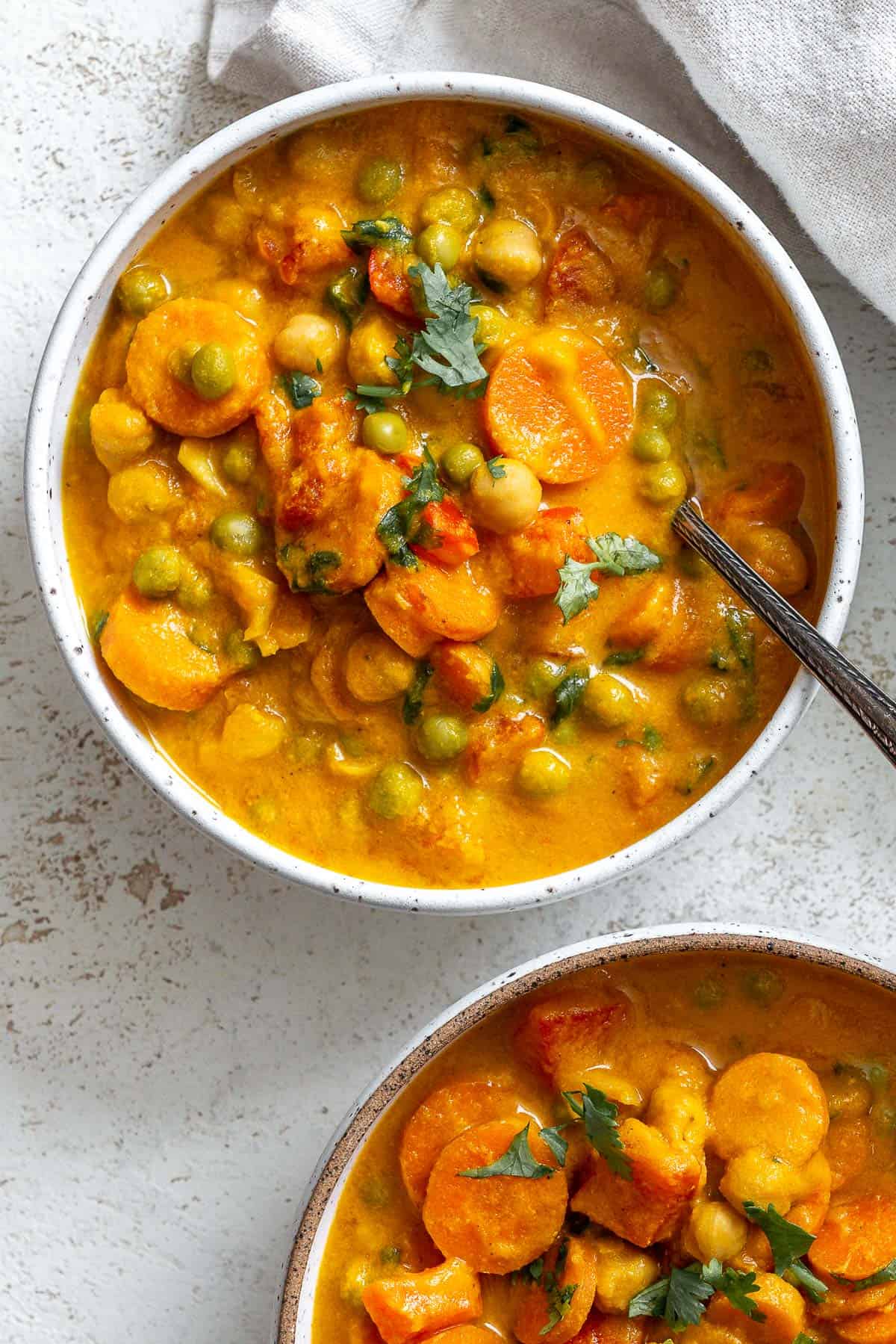 Two bowls of completed Creamy Chickpea and Carrot Curry in a bowl against a white surface.
