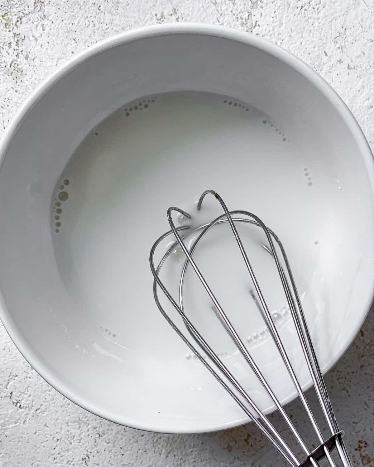 process s،t of whisking ingredients in a white bowl