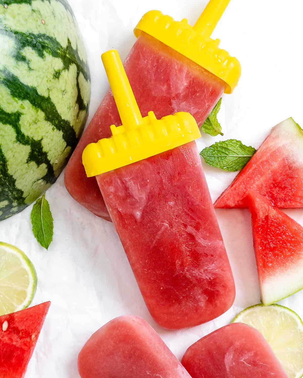 two completed Watermelon Popsicles with watermelon ،tered in the background