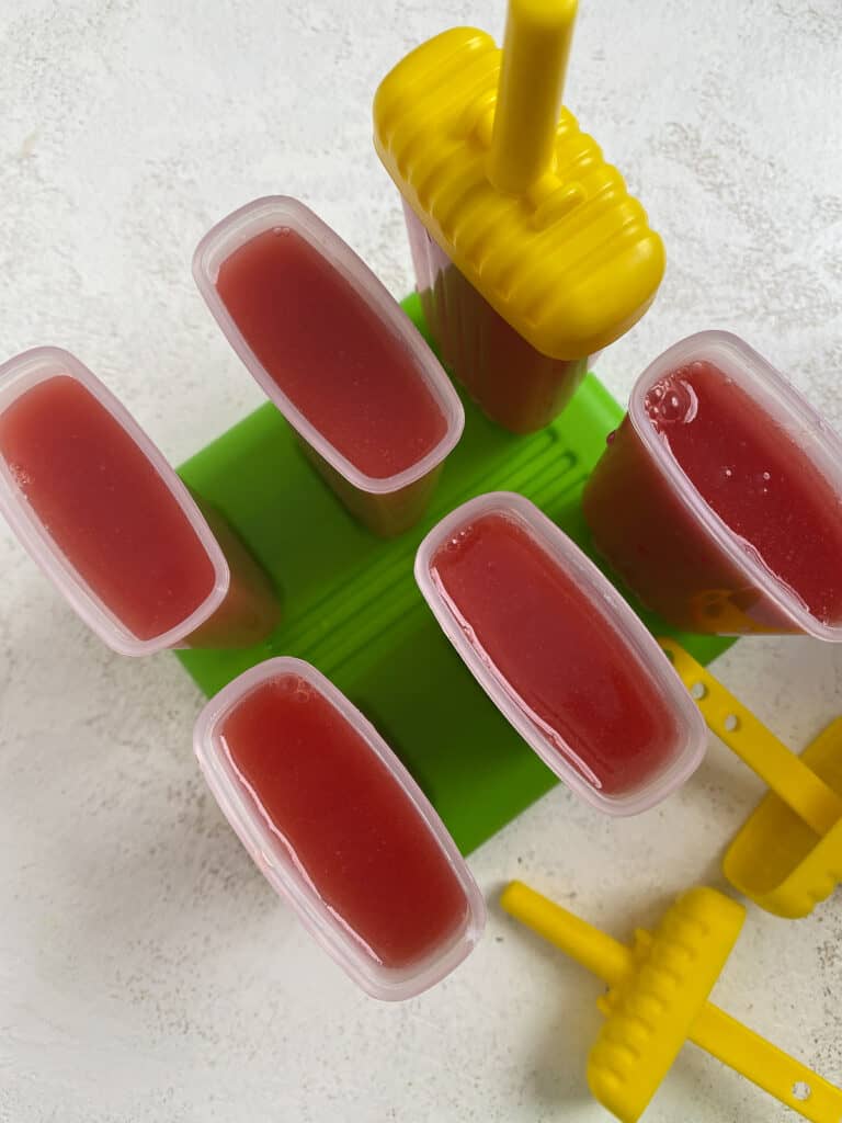 6 watermelon popsicles in their molds against a light background