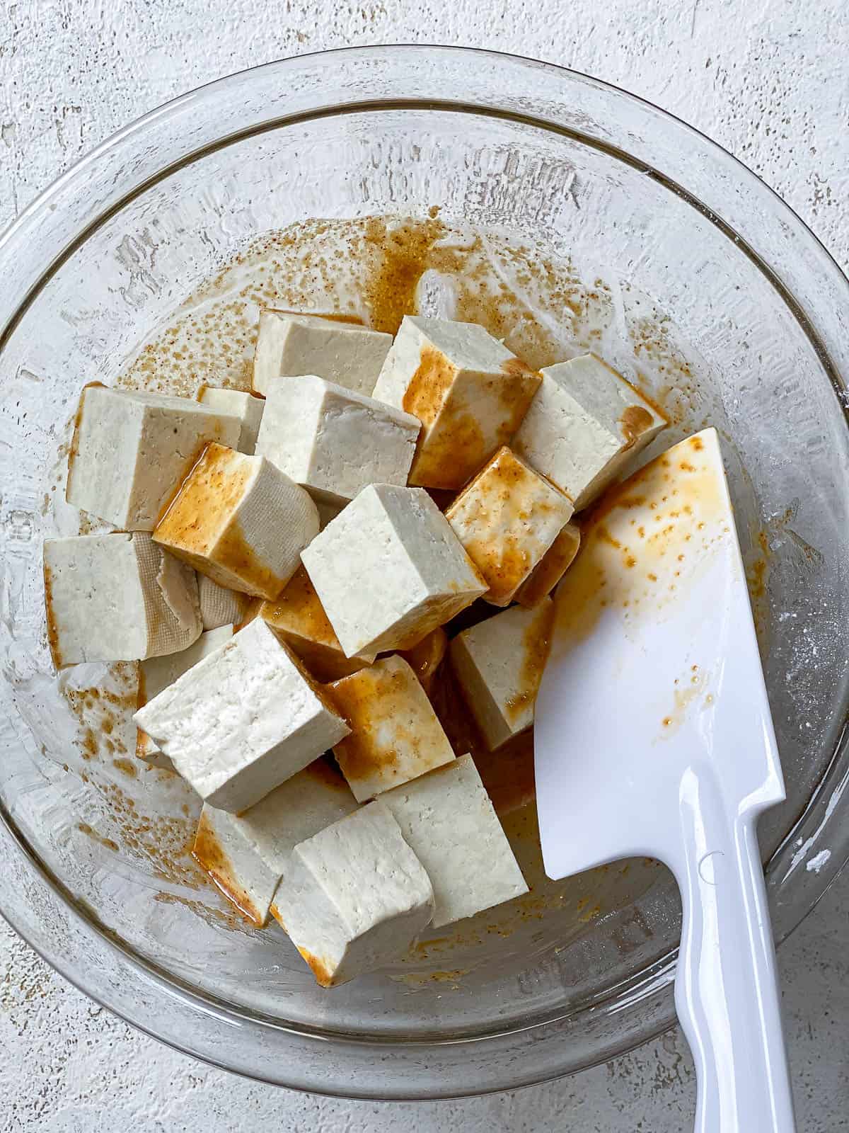 Tofu cubes in a bowl being tossed to coat well.