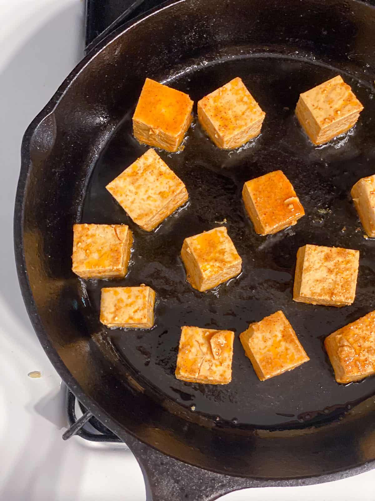 Marinated tofu in a single layer on a cast iron pan.