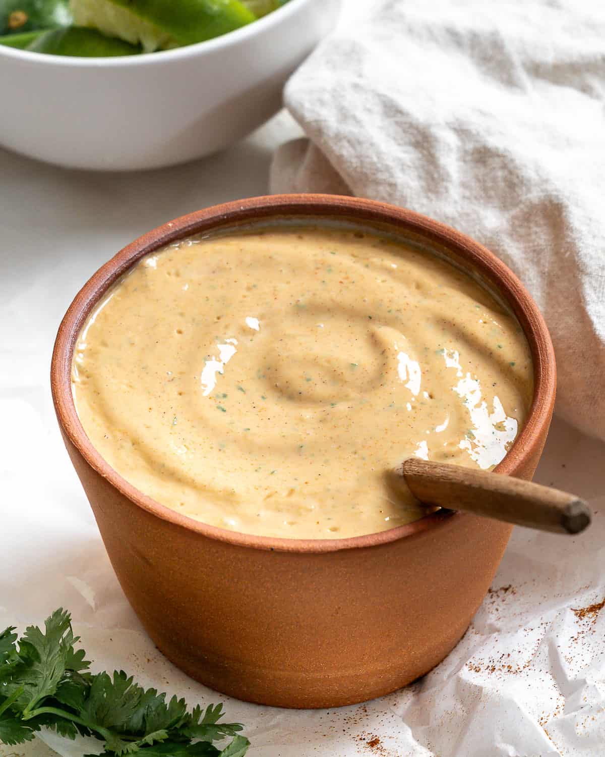 Taco salad dressing in a terracotta bowl with a wooden spoon. Cilantro is on the bottom left. A gray napkin in the top right corner.